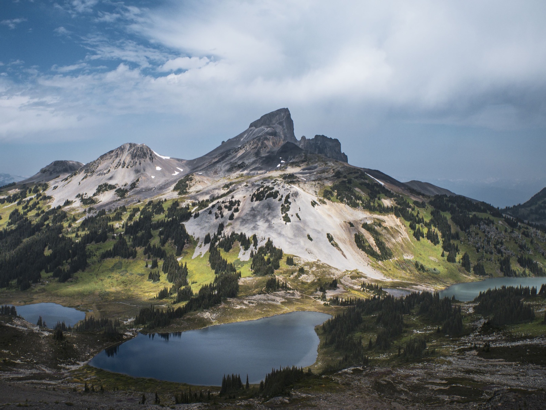 The dark summit of Black Tusk above green alpine slopes and blue lakes, viewed from Panorama Ridge
