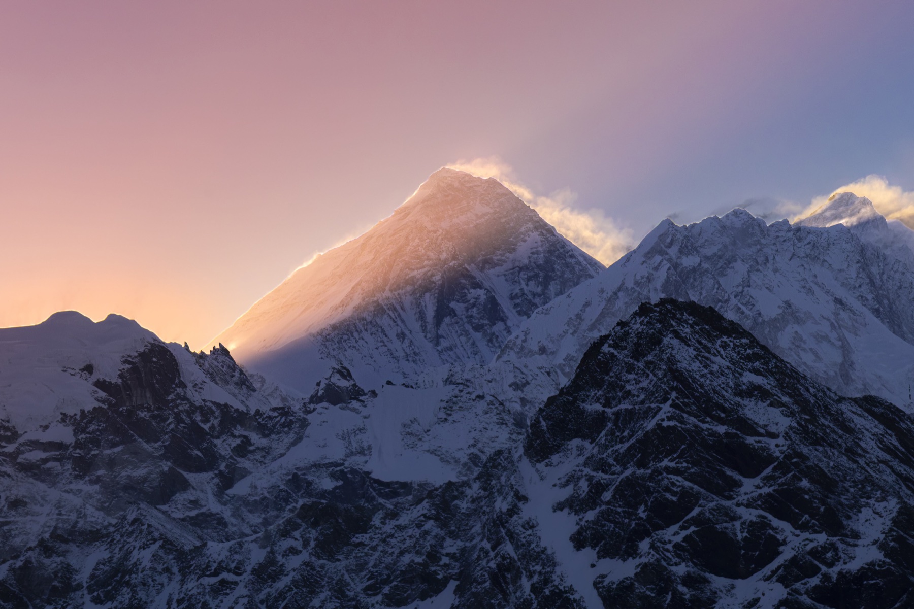 Golden light and windblown snow along Everest’s summit above dark Himalayan ridges